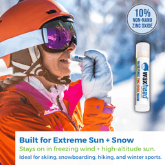 A woman applying Waxhead Zinc Oxide Lip Balm while skiing, showcasing its protective qualities against extreme weather.