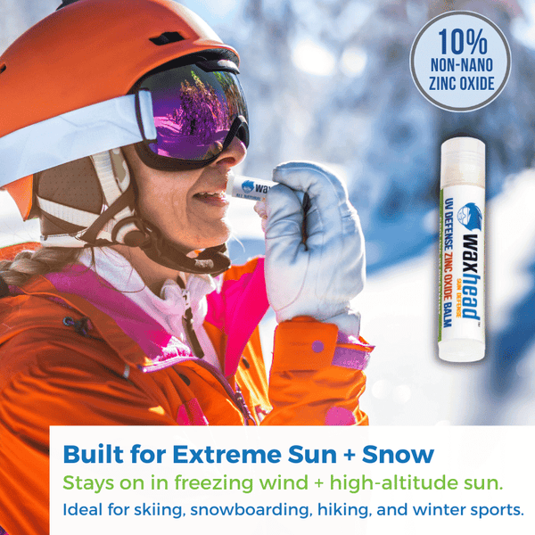 A woman applying Waxhead Zinc Oxide Lip Balm while skiing, showcasing its protective qualities against extreme weather.