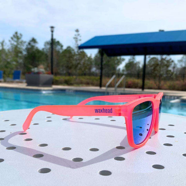 Pink Polarized Sunglasses by Waxhead on a table near a pool, showcasing vibrant colors and stylish design.