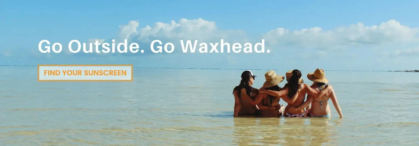 A beach scene with four women sitting in shallow water, seen from behind, under a blue sky with clouds. Large white text reads 'Go Outside.